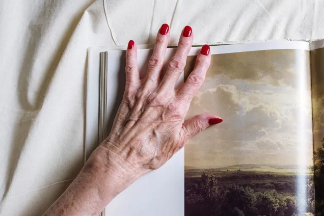 A photo of a hand with reumatism with red painted nails positioned on top of a photography book.